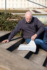 Image showing Man sitting on steps reading a newspaper