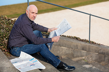 Image showing Man sitting on steps reading a newspaper