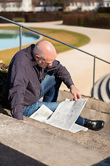 Image showing Man sitting on steps reading a newspaper