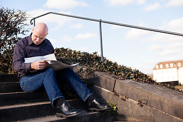 Image showing Man sitting on steps reading a newspaper