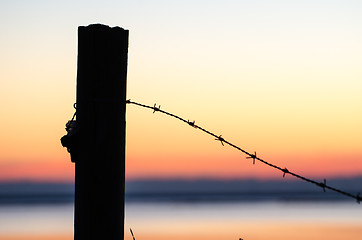 Image showing Silhouette of barb wire at a post