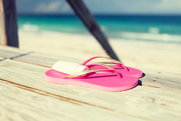 Image showing close up of sunscreen and slippers at seaside