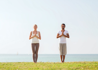 Image showing smiling couple making yoga exercises outdoors