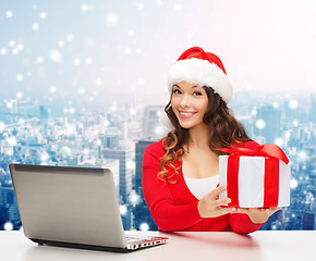 Image showing smiling woman in santa hat with gift and laptop