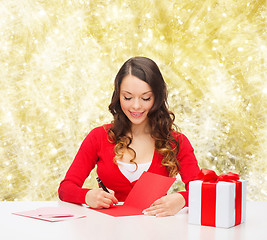 Image showing smiling woman with gift box writing letter