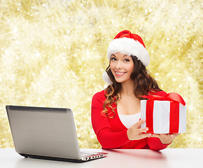 Image showing smiling woman in santa hat with gift and laptop