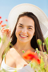 Image showing smiling young woman in straw hat on poppy field