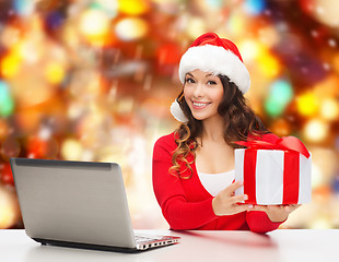 Image showing smiling woman in santa hat with gift and laptop