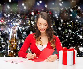 Image showing smiling woman with gift box writing letter