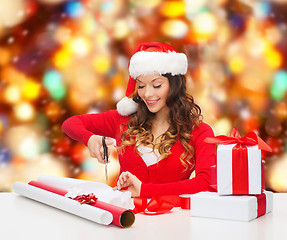 Image showing smiling woman in santa helper hat packing gift box