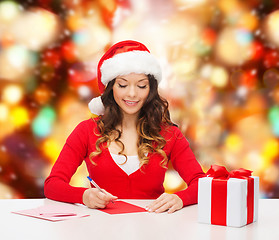 Image showing smiling woman with gift box writing letter