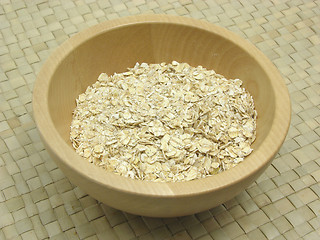 Image showing Wooden bowl with oat flakes on rattan underlay