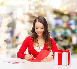 Image showing smiling woman with gift box writing letter