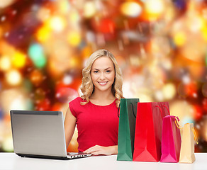 Image showing smiling woman in red shirt with gifts and laptop