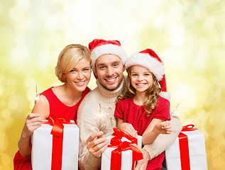 Image showing smiling family holding gift boxes and sparkles