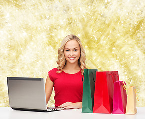 Image showing smiling woman in red shirt with gifts and laptop