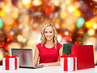 Image showing smiling woman in red shirt with gifts and laptop