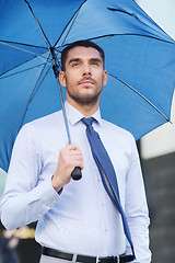 Image showing young serious businessman with umbrella outdoors