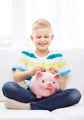 Image showing smiling little boy with piggy bank at home