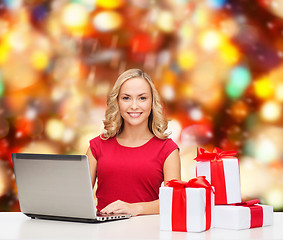 Image showing smiling woman in red shirt with gifts and laptop