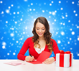 Image showing smiling woman with gift box writing letter