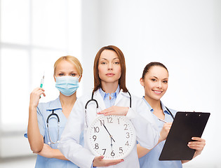 Image showing calm female doctor and nurses with wall clock