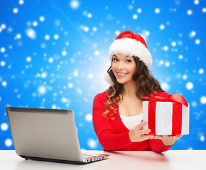 Image showing smiling woman in santa hat with gift and laptop