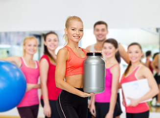 Image showing smiling sporty woman with jar of protein