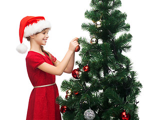 Image showing smiling girl in santa helper hat decorating a tree