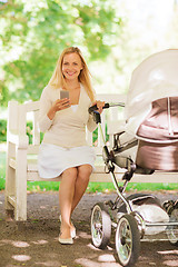 Image showing happy mother with smartphone and stroller in park