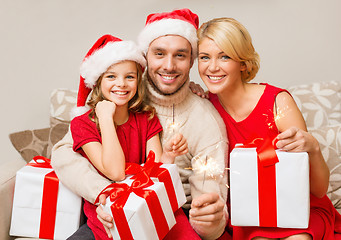 Image showing smiling family holding gift boxes and sparkles