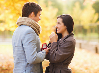 Image showing smiling couple with red gift box in autumn park