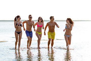 Image showing smiling friends in sunglasses running on beach