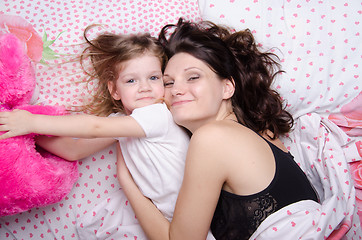 Image showing Daughter reaches for a soft toy lying with her mother