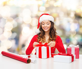 Image showing smiling woman in santa helper hat packing gifts