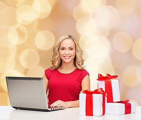 Image showing smiling woman in red shirt with gifts and laptop