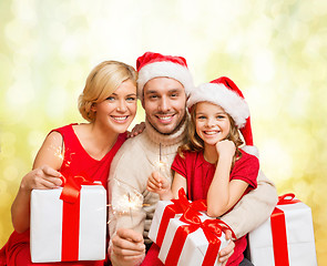 Image showing smiling family holding gift boxes and sparkles