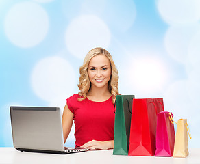 Image showing smiling woman in red dress with gifts and laptop