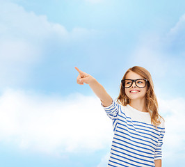 Image showing cute little girl in eyeglasses pointing in the air