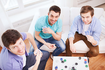 Image showing three smiling male friends playing cards at home