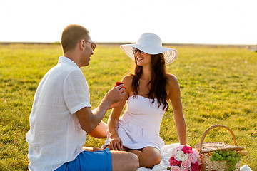 Image showing smiling couple with small red gift box on picnic