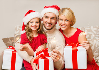 Image showing smiling family holding gift boxes and sparkles