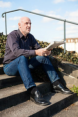 Image showing Man sitting on steps reading a newspaper