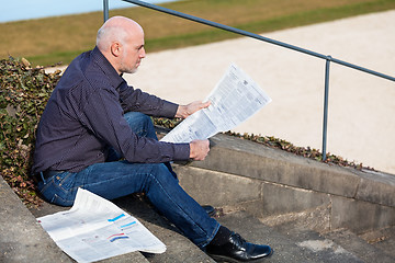 Image showing Man sitting on steps reading a newspaper