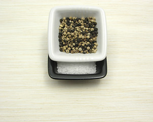 Image showing Bowls of chinaware with peppercorns and salt on beige underlay