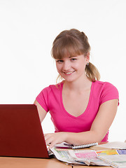 Image showing Girl with laptop and newspaper sitting at table