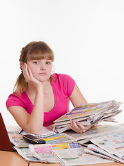 Image showing Girl sitting with a pile of newspapers at table