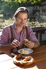 Image showing Attractive man eats traditional cheese with pretzel in a Bavaria