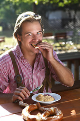 Image showing Attractive man eats traditional cheese with pretzel in a Bavaria