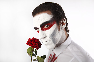 Image showing Man with white mascara and bloody shirt holds red rose